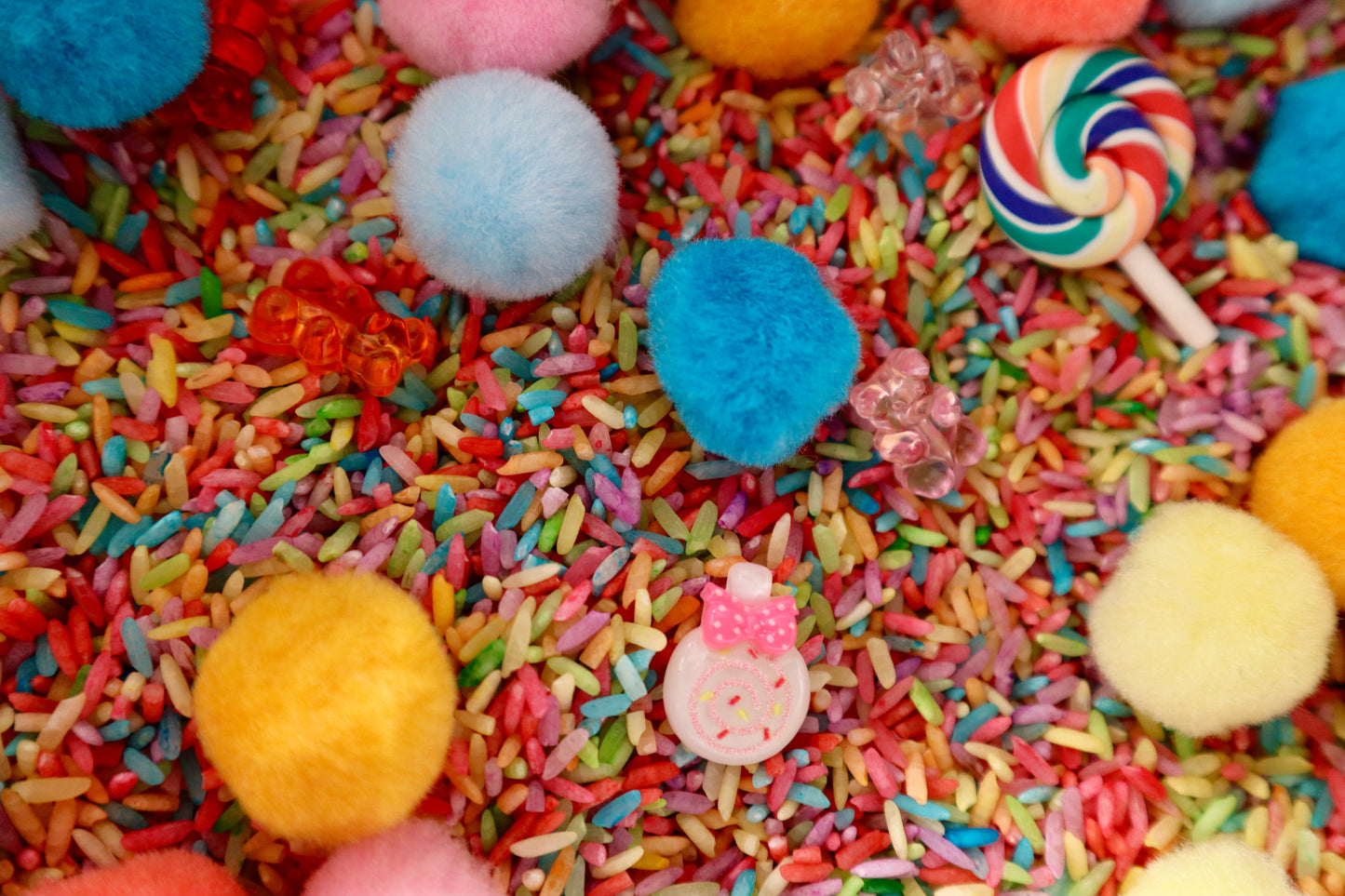 Colorful sprinkles with candy and pom-poms on a surface